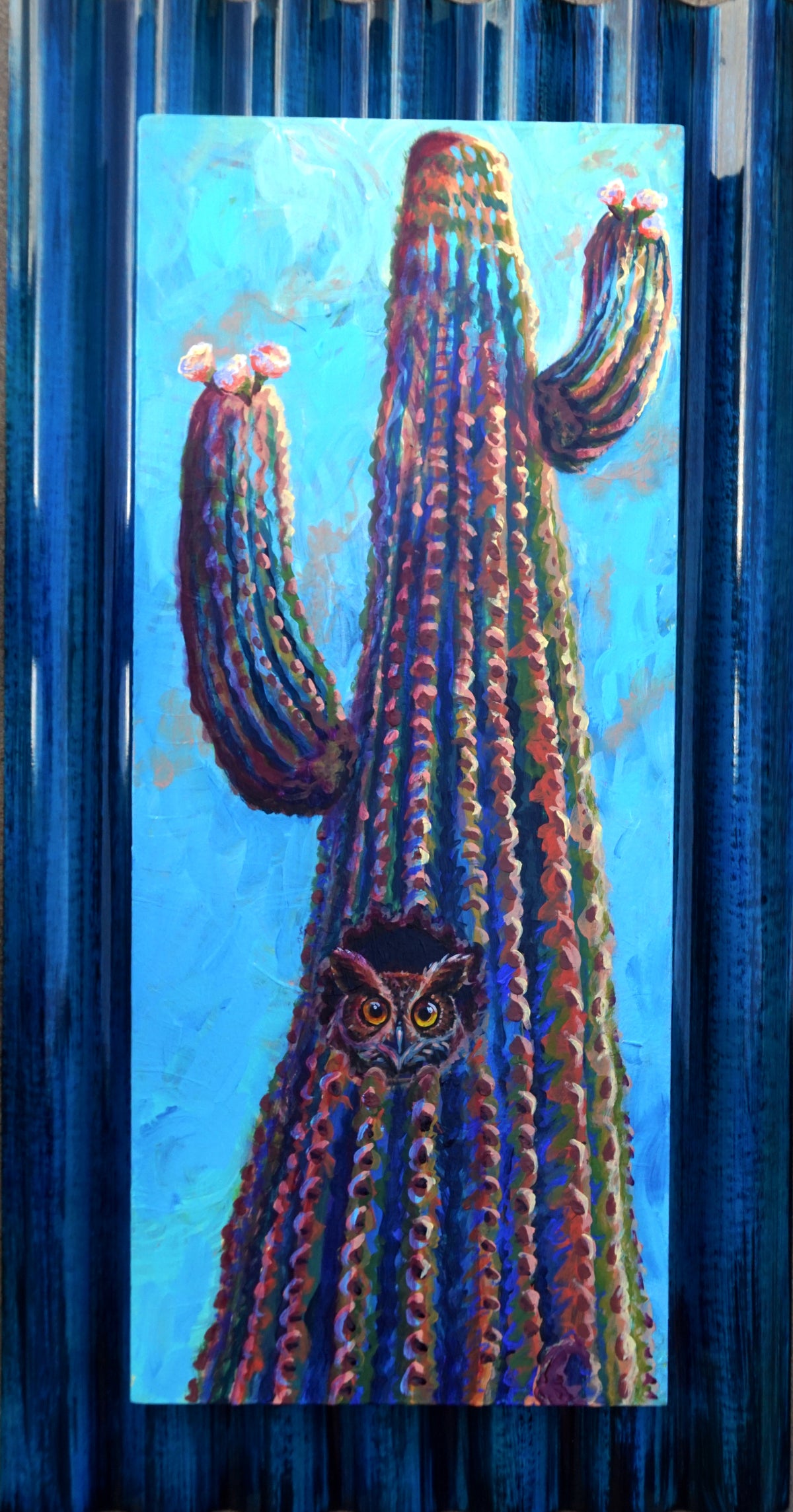 Great horned owl peeking from a saguaro cactus cavity, painted on a reclaimed cabinet door mounted on blue corrugated tin